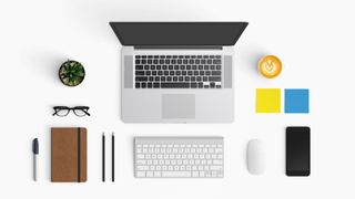 A white laptop sitting open on a table with various office supplies and items around it